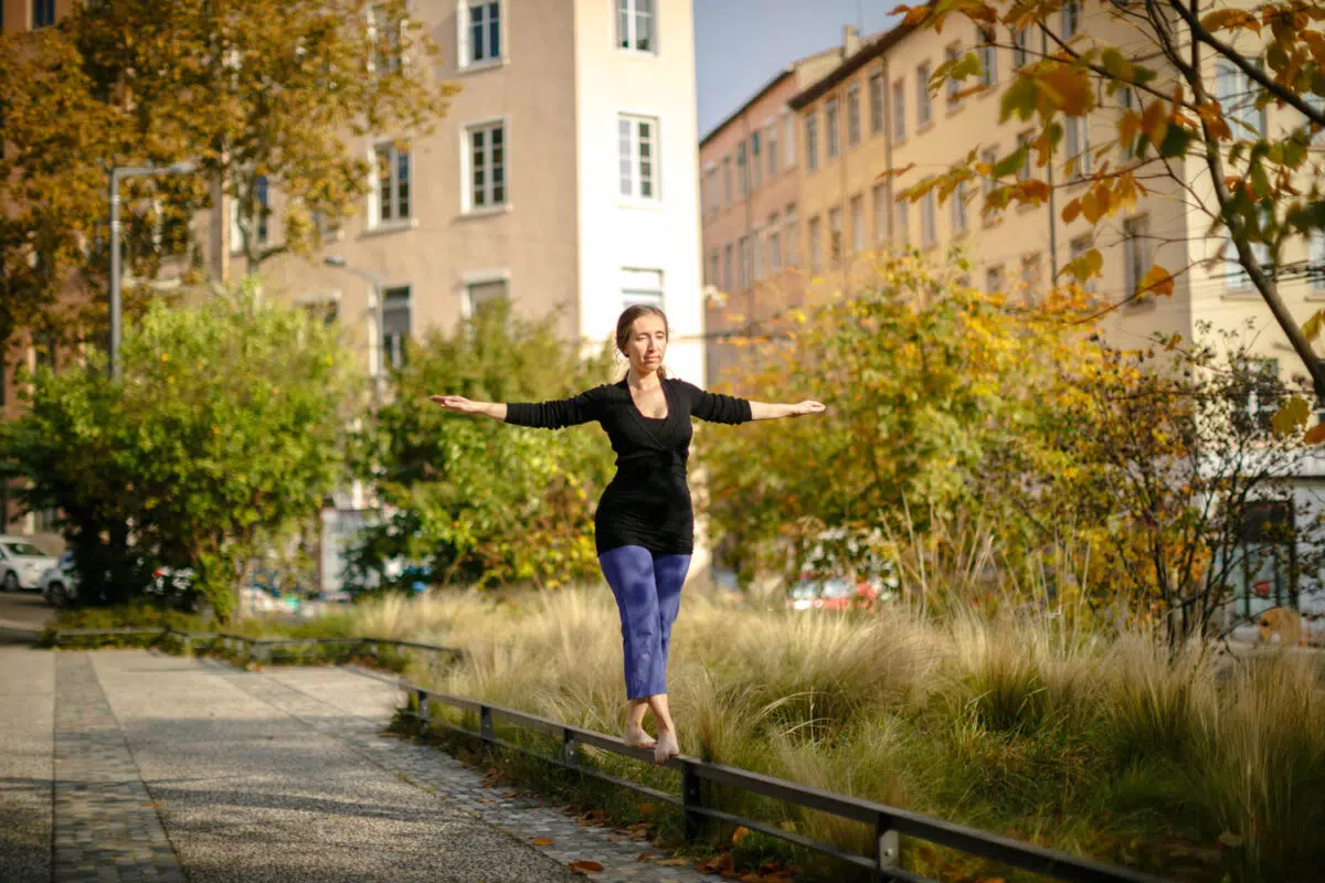 Femme en équilibre sur une bordure, bras ouverts, dans un jardin en automne