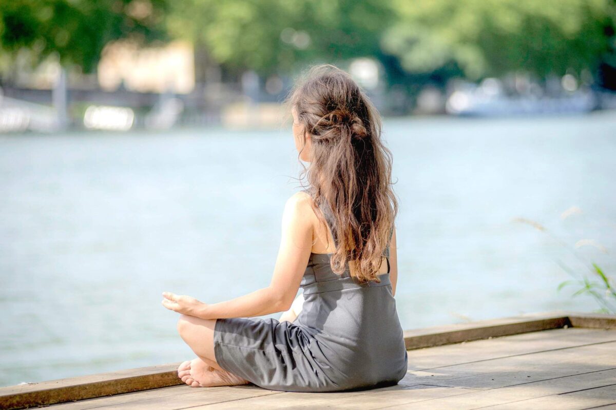 Femme en méditation assise au bord de l'eau, vue de dos