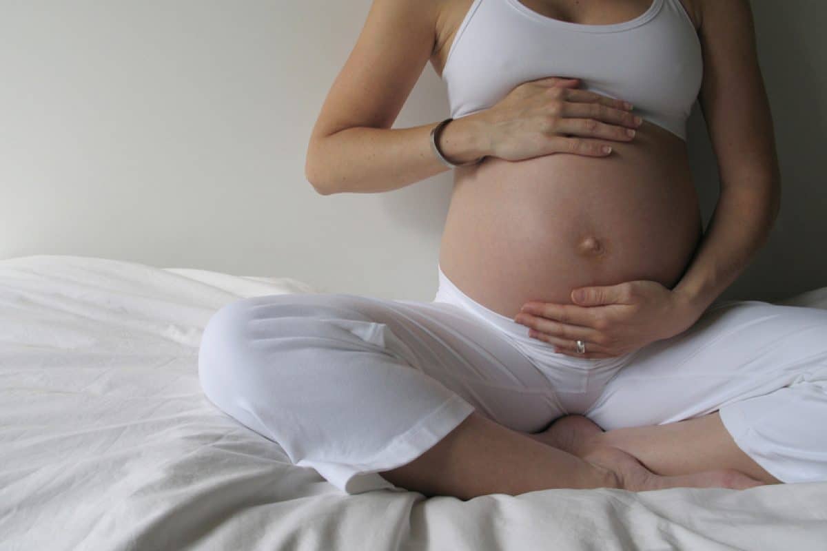 Femme enceinte assise en tailleur, mains posées sur son ventre