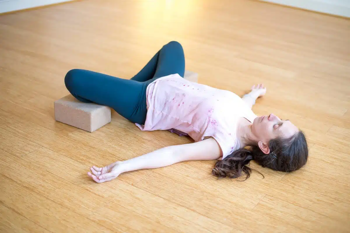 Femme allongée en torsion douce, jambes posées sur une brique de yoga, en yin yoga