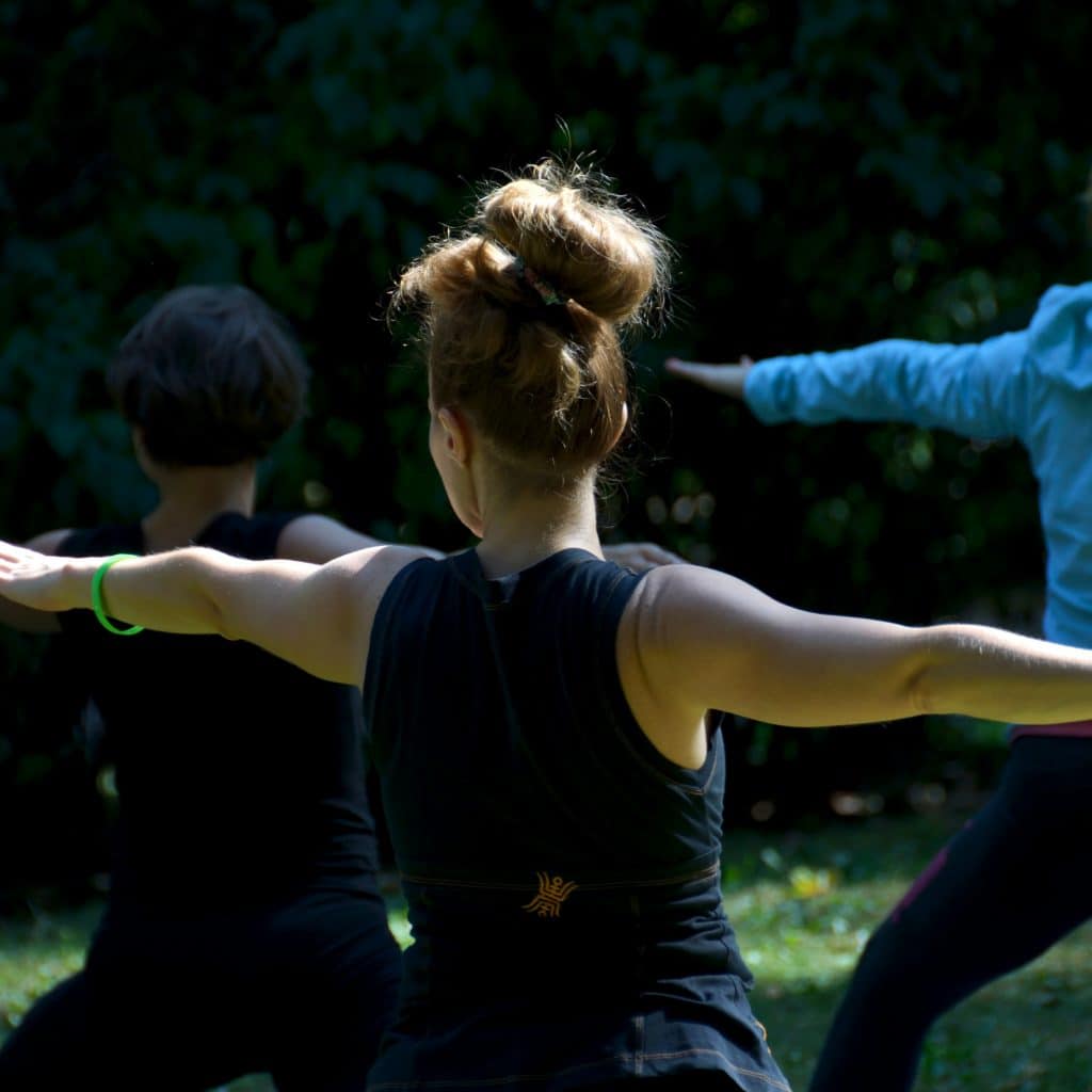 Groupe en posture du guerrier 2, bras tendus, lors d'une séance de yoga en plein air