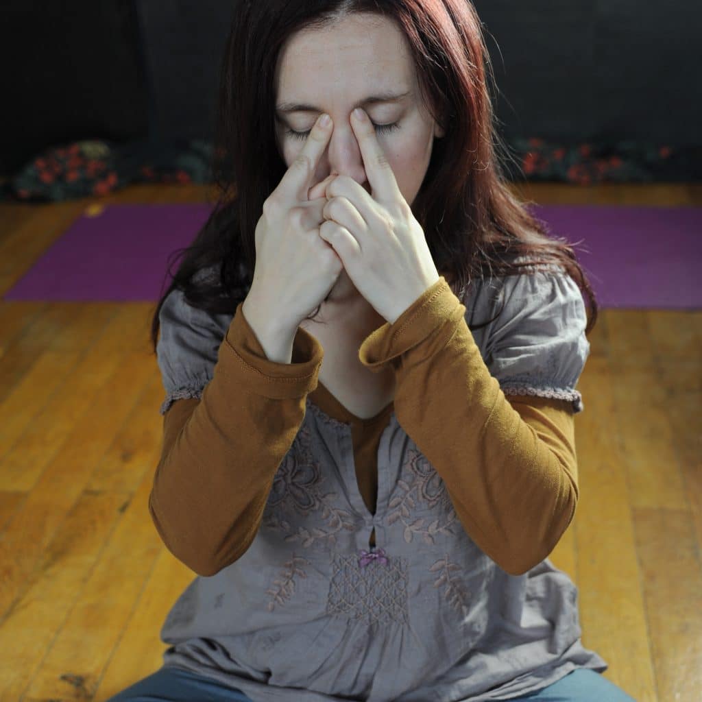 Femme assise en tailleur pratiquant un exercice de yoga du visage, doigts sur l'arête du nez