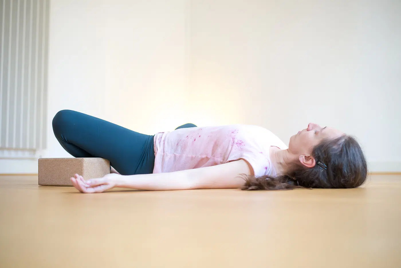 Femme allongée en relaxation, jambes posées sur une brique de yoga