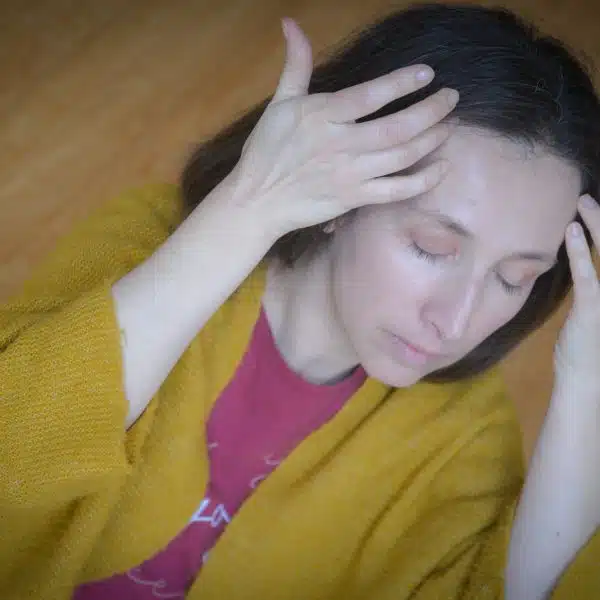 Femme en gilet jaune massant son front du bout des doigts, en yoga du visage