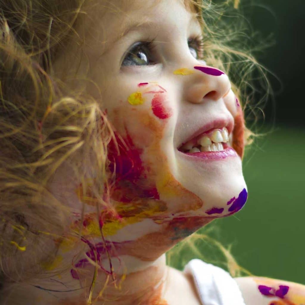 Enfant souriante au visage barbouillé de peinture, regard vers le ciel