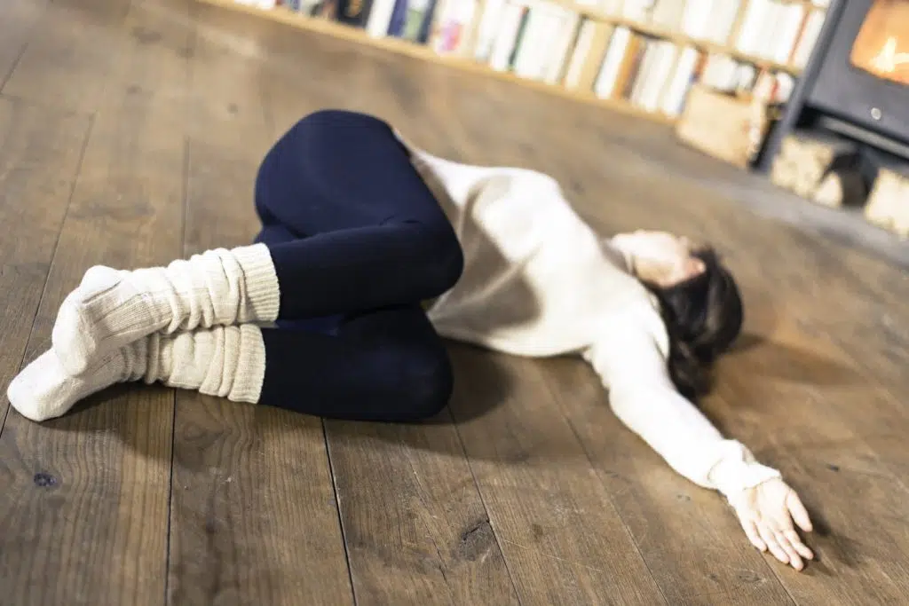 Femme allongée en torsion au sol, genoux repliés, dans un salon chaleureux en hiver