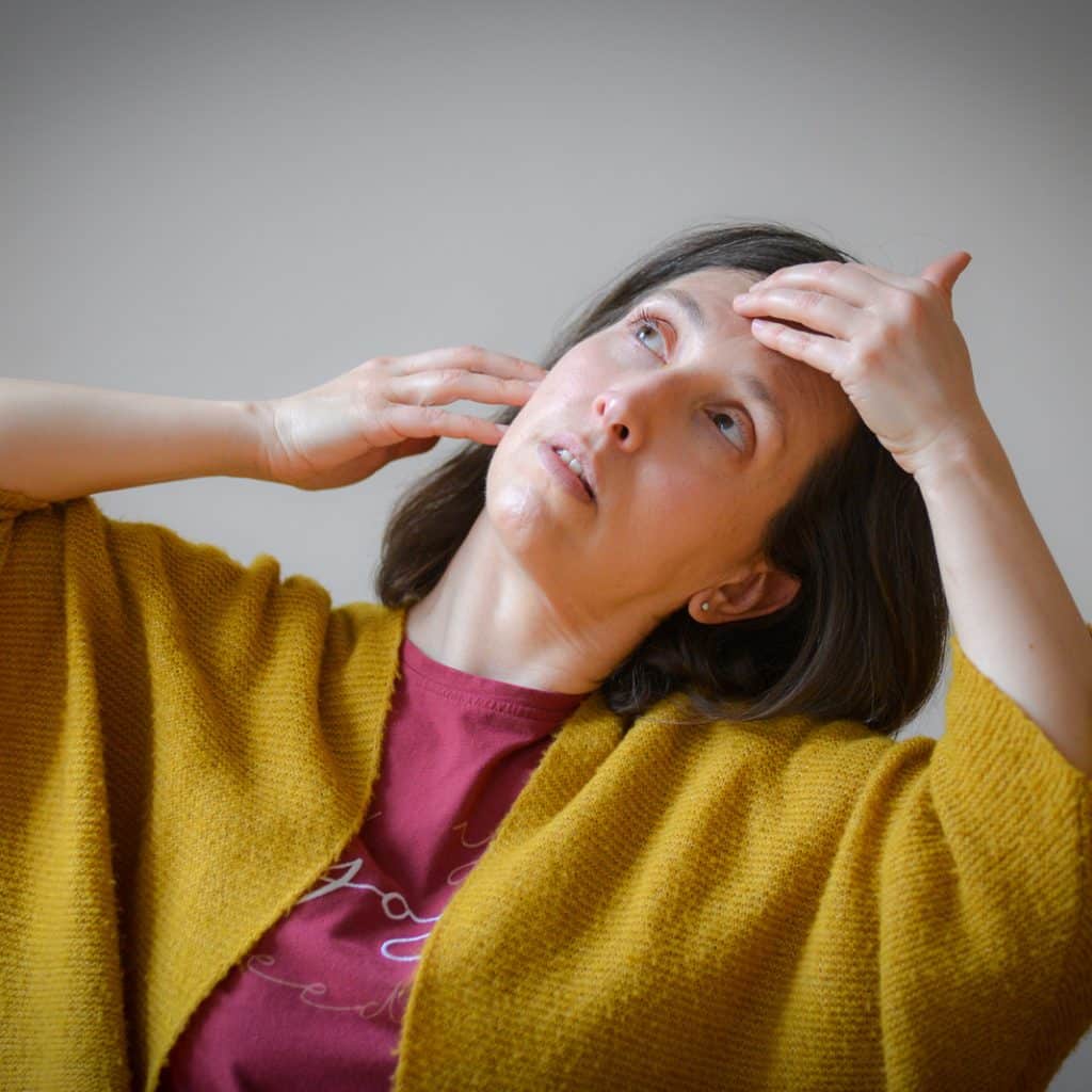 Femme en gilet jaune lissant son front du bout des doigts, en yoga du visage