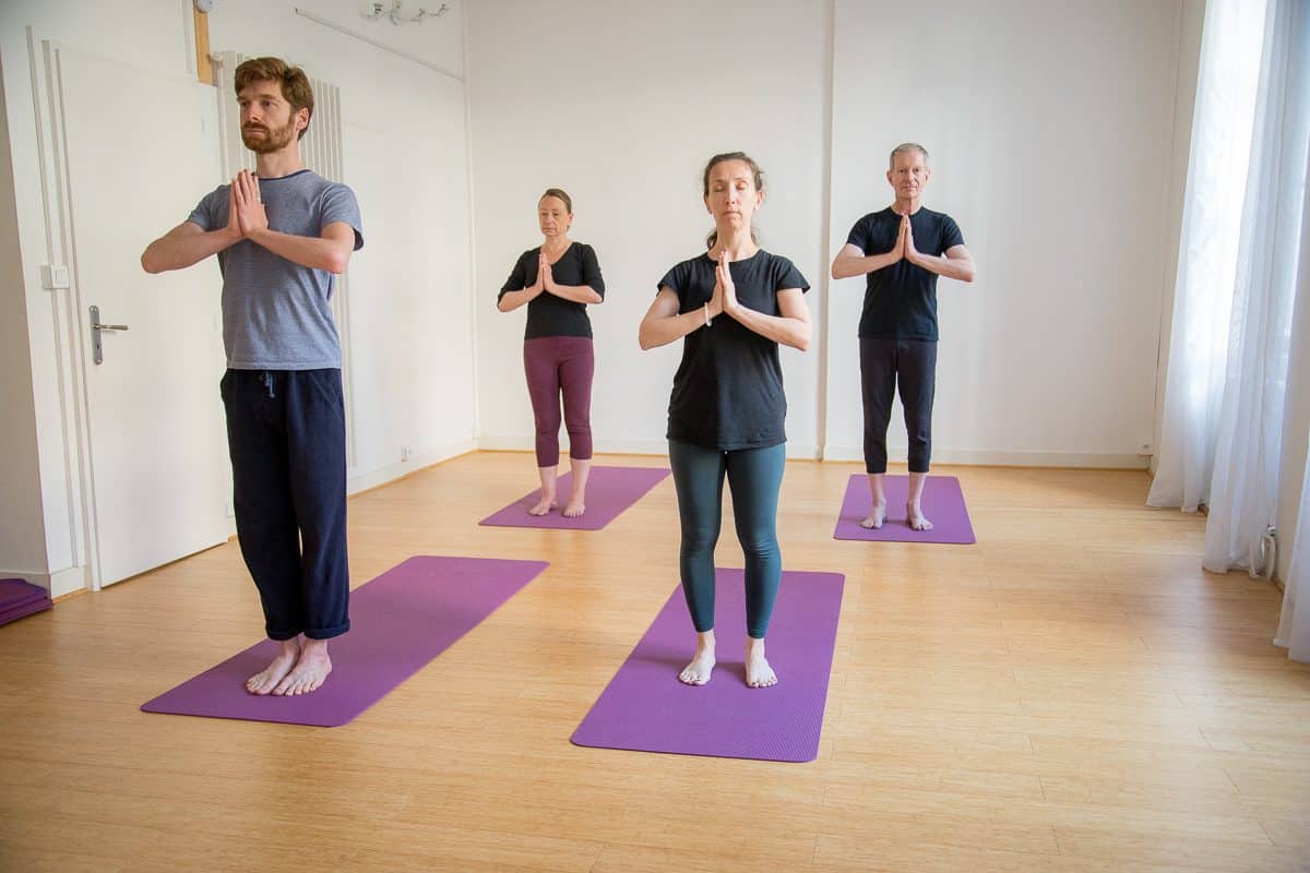 Élèves debout en posture de la montagne, mains jointes, lors d'un cours de yoga pour débutants