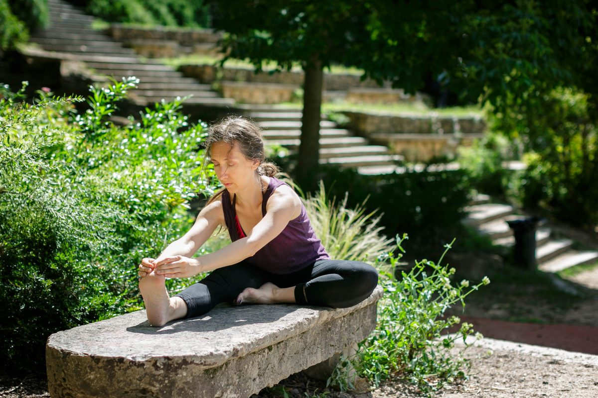 Femme en flexion avant assise sur un banc de pierre, dans un jardin verdoyant