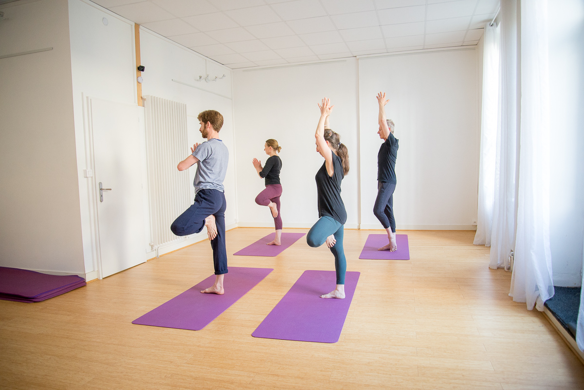 Élèves en posture de l'arbre, bras levés, dans une salle de cours de yoga à Lyon