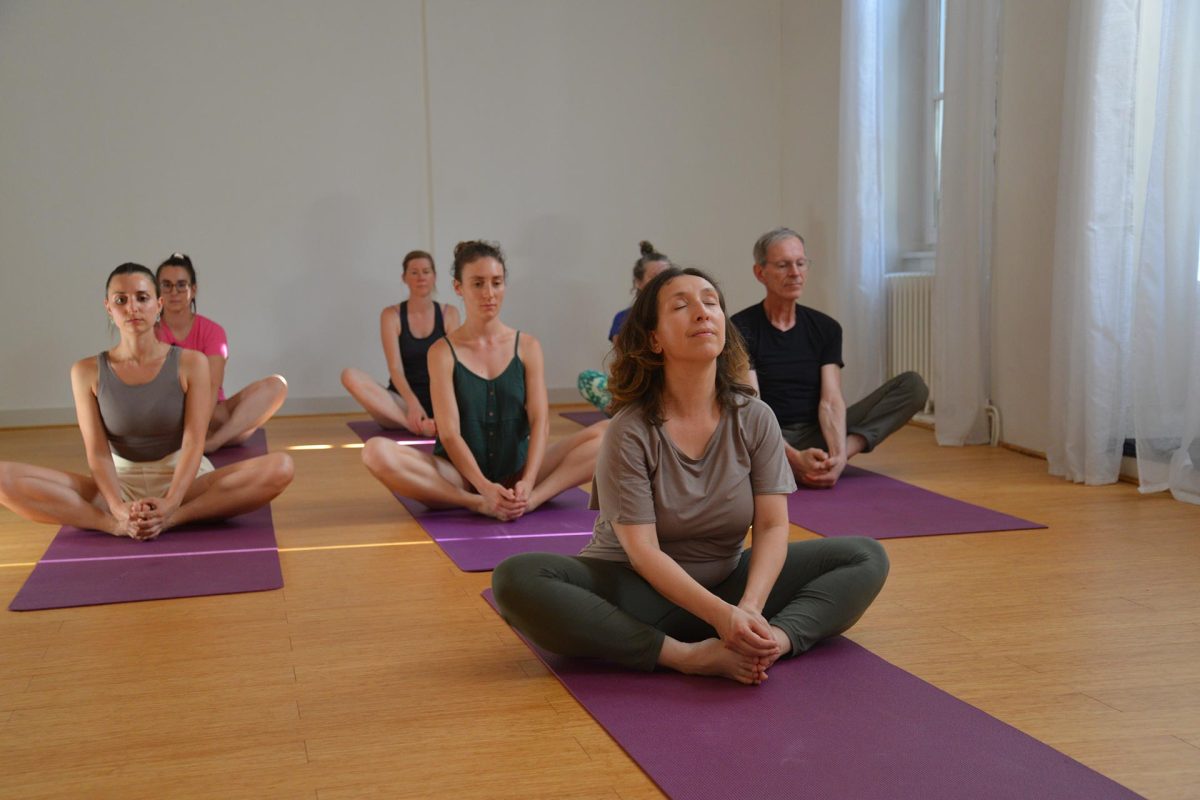 Élèves assis en tailleur, yeux fermés, pendant une séance de yoga à Lyon