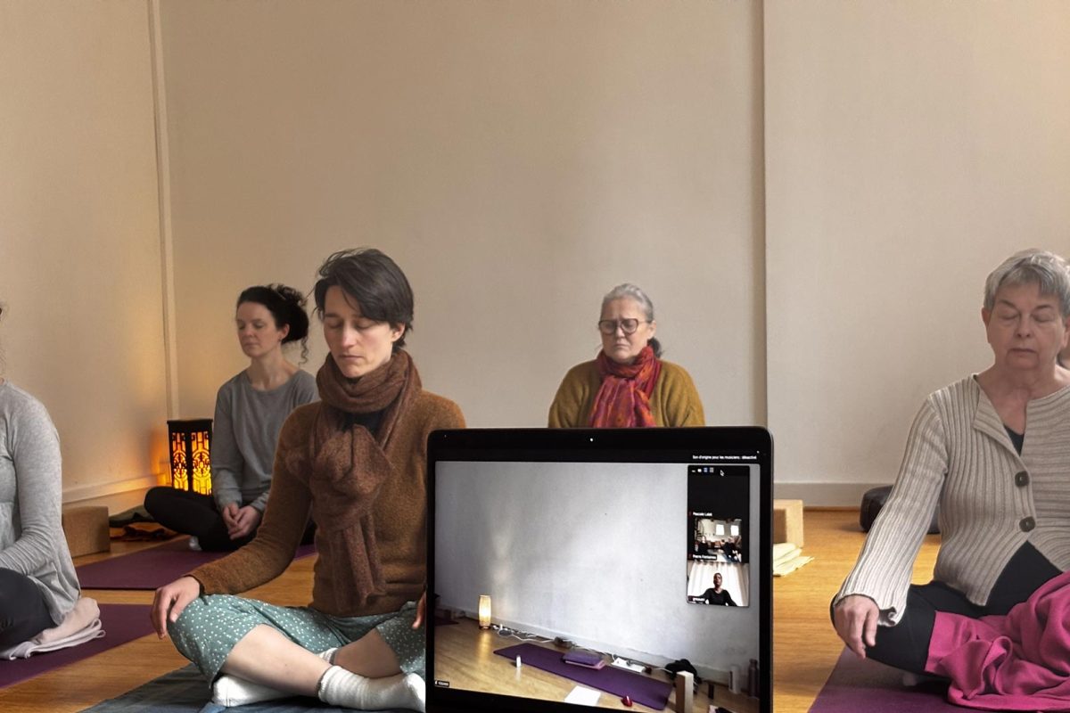 Élèves en méditation assise autour d'un ordinateur, pendant un cours de yoga en ligne en direct