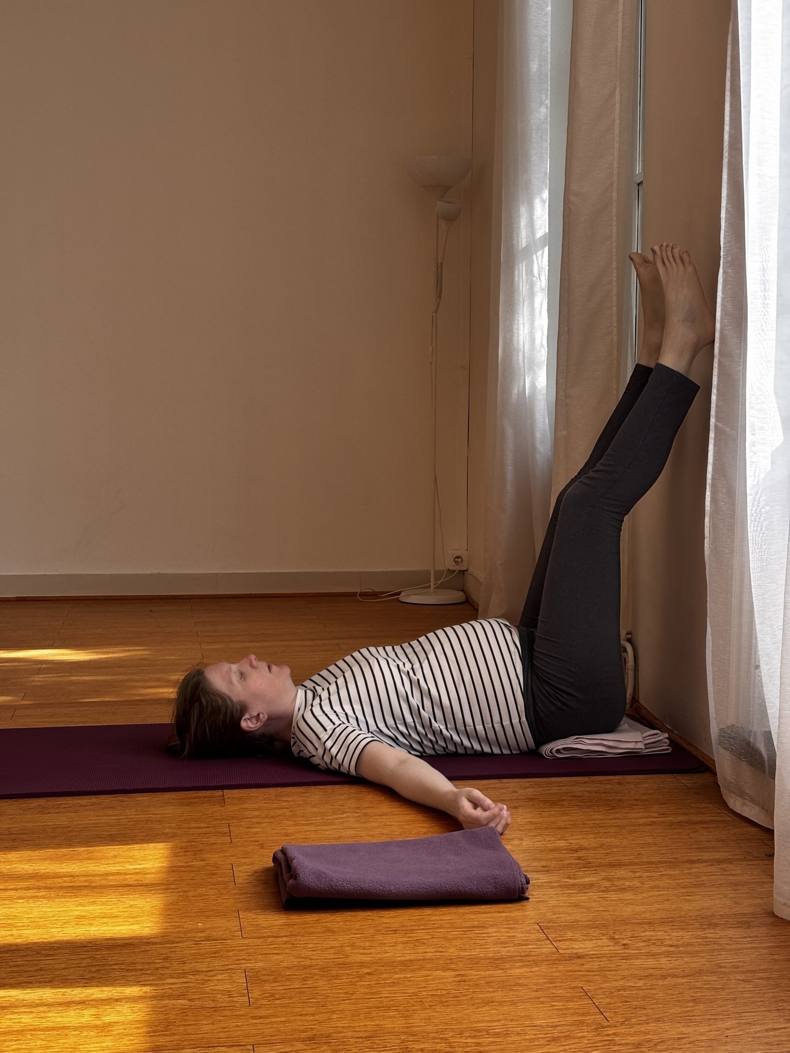 Femme enceinte allongée, jambes contre le mur, en posture de yoga prénatal